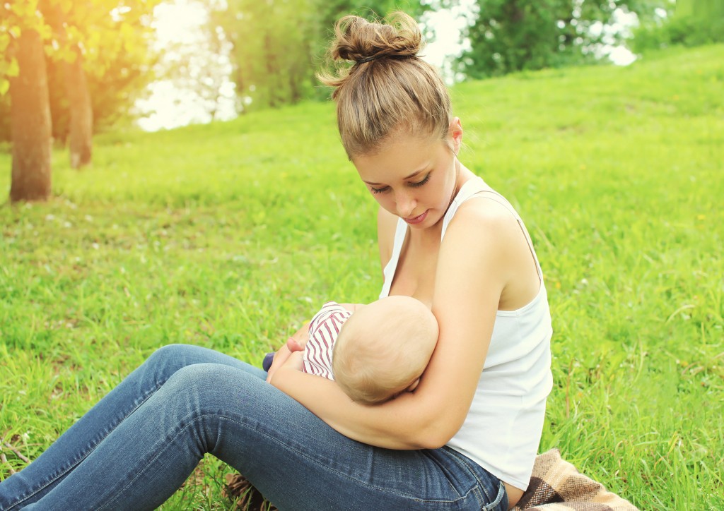 Mother feeding breast baby on the grass in summer day